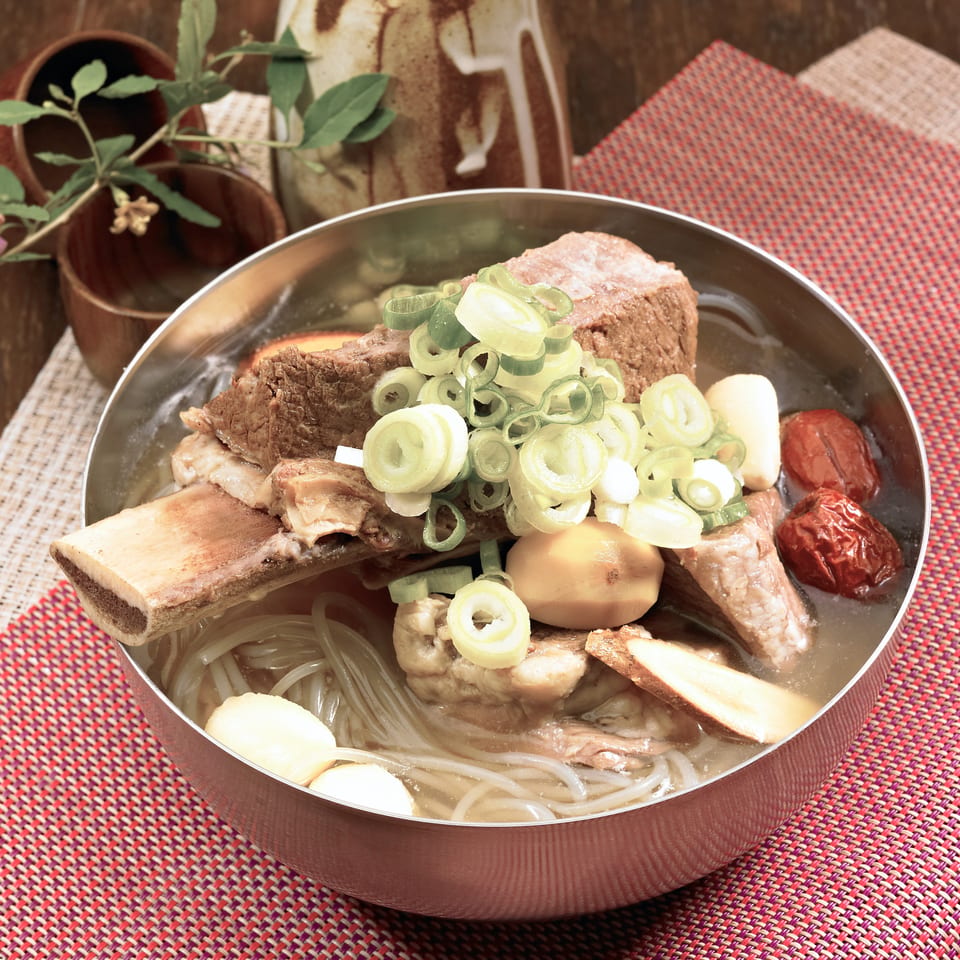 Korean Galbitang, a beef short rib soup with noodles, jujubes, and green onions in a metal bowl.