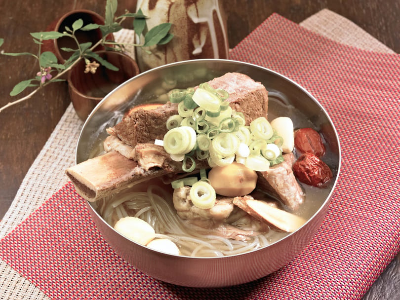 Korean Galbitang, a beef short rib soup with noodles, jujubes, and green onions in a metal bowl.