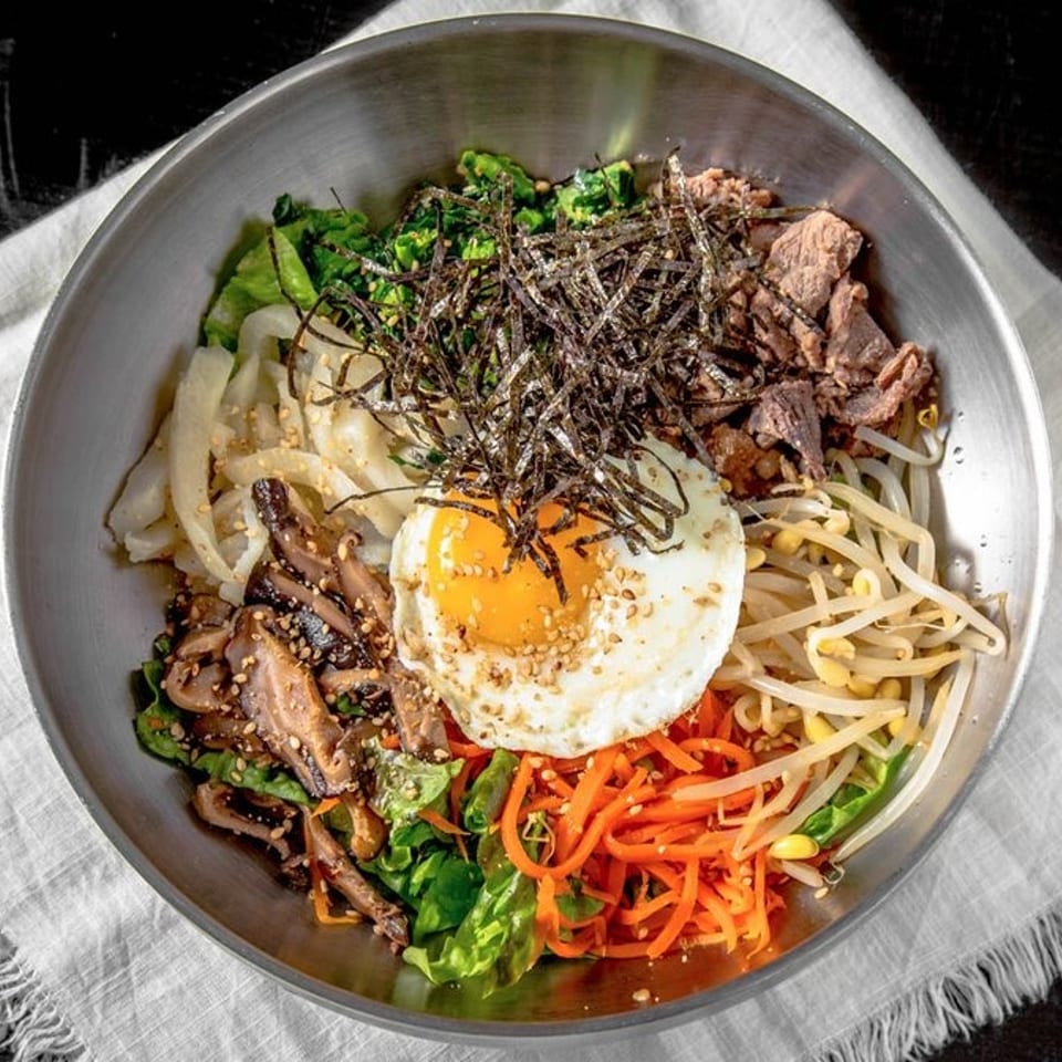 A colorful bibimbap bowl with beef, vegetables, and a fried egg, on a white napkin.