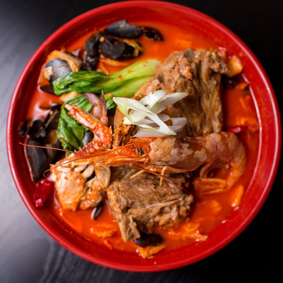 Spicy seafood and meat stew in a red bowl, garnished with green onions.