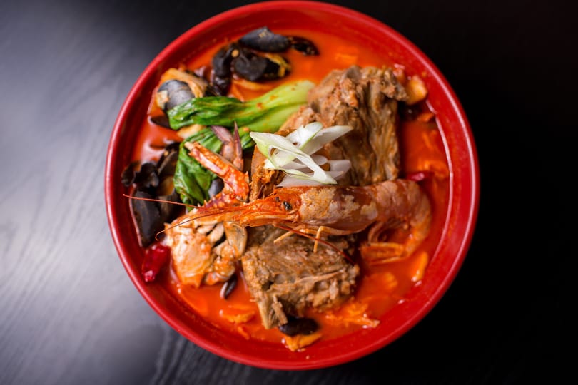 Spicy seafood and meat stew in a red bowl, garnished with green onions.