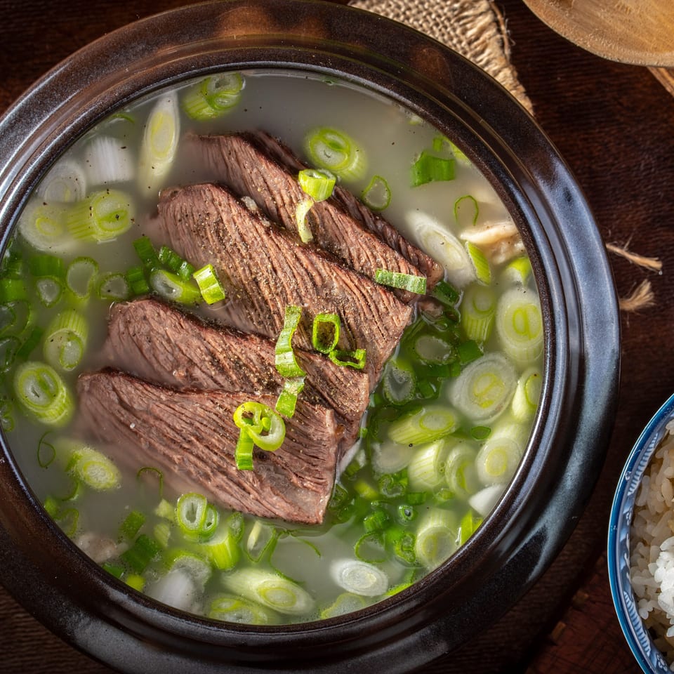 Close-up of Korean beef short rib soup (Galbitang) with green onions and a side of rice.