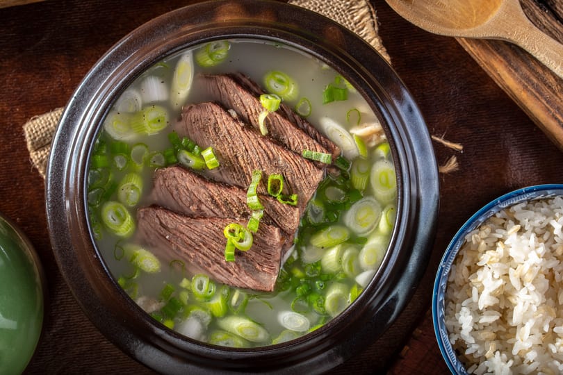 Close-up of Korean beef short rib soup (Galbitang) with green onions and a side of rice.